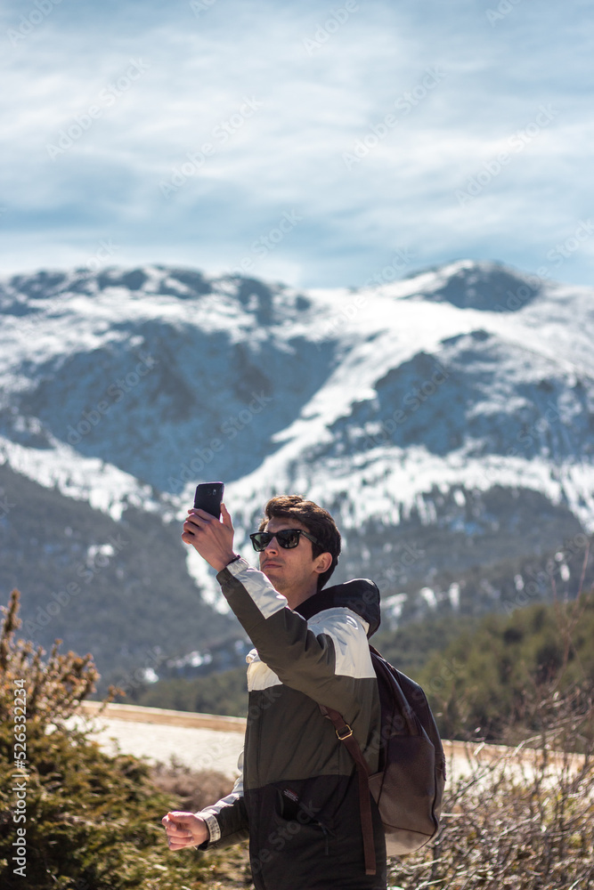 Handsome caucasian man posing to camera. He carries his cell phone and sunglasses. he has snowy mountains in the background Handsome caucasian man posing to camera. He carries his cell phone and sunglasses. he has snowy mountains in the background