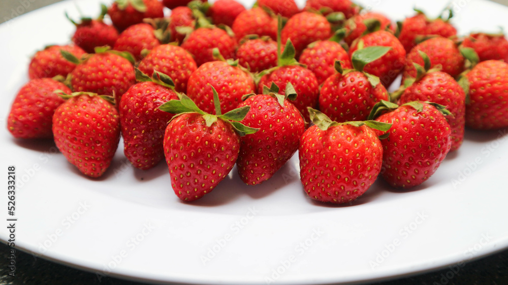 Fresh red strawberries with leaves on white plate Fresh red strawberries with leaves on white plate