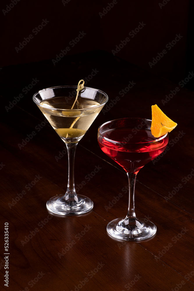 two cocktail glasses with martini, olive and orange on rubber stand on pub counter viewed from an angle