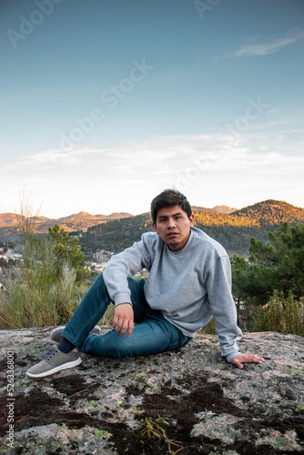 Latin american handsome guy sitting in rock in nature. With the mountains in the background