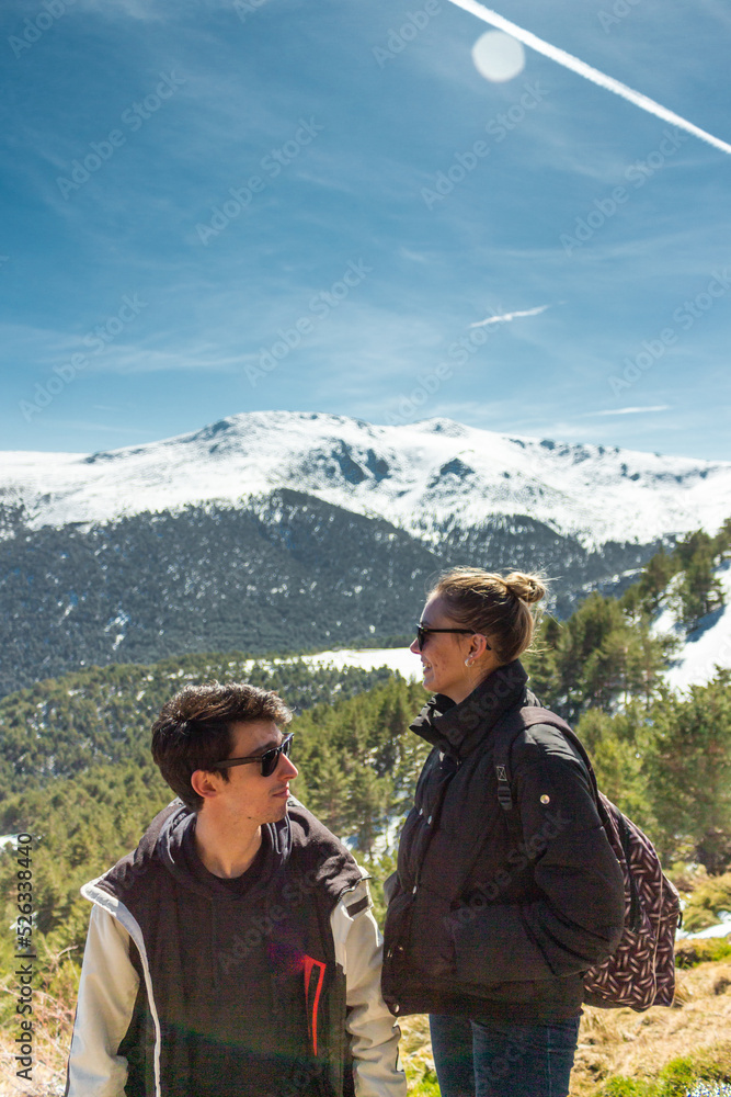 Beautiful friends with sun glasses posing in the middle of a snowy of a pine forest. They are smiling and looking away