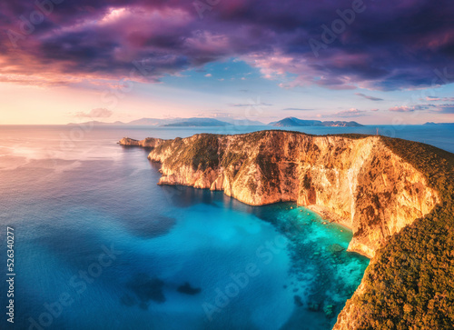 Aerial view of beautiful mountain, blue sea at colorful sunset in summer. Landscape with rocky coast, forest, sea bay, beach, azure water, purple sky. Top view of cliffs. Cape Lefkada, Greece. Nature