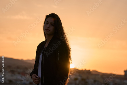 young hispanic girl posing at the rocks of a beach in the mediterranean sea while sunrise