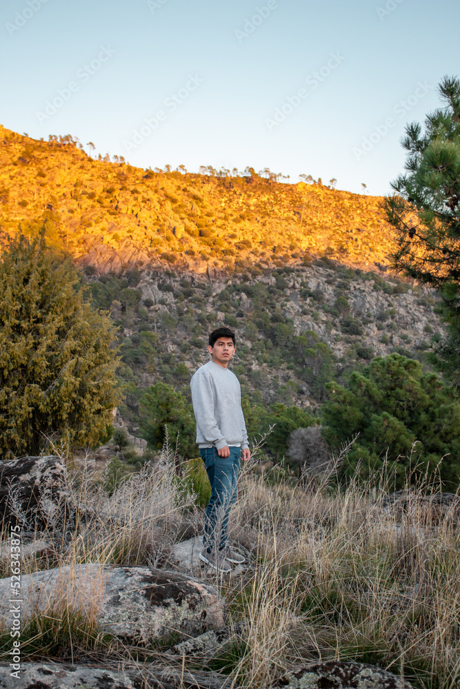 Naklejka premium Latin american handsome guy sitting in rock in nature. With the mountains in the background