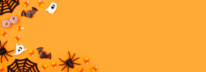 Halloween corner border of scattered candy and decor. Above view over an orange banner background with copy space.