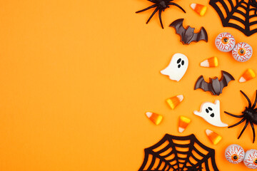 Halloween side border of scattered candy and decor. Overhead view over an orange background with copy space.