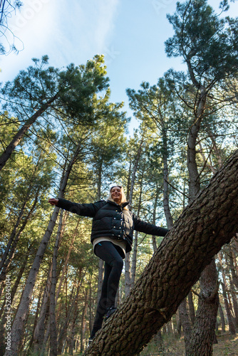blonde woman walking on top of a pine trunk in the middle of nature