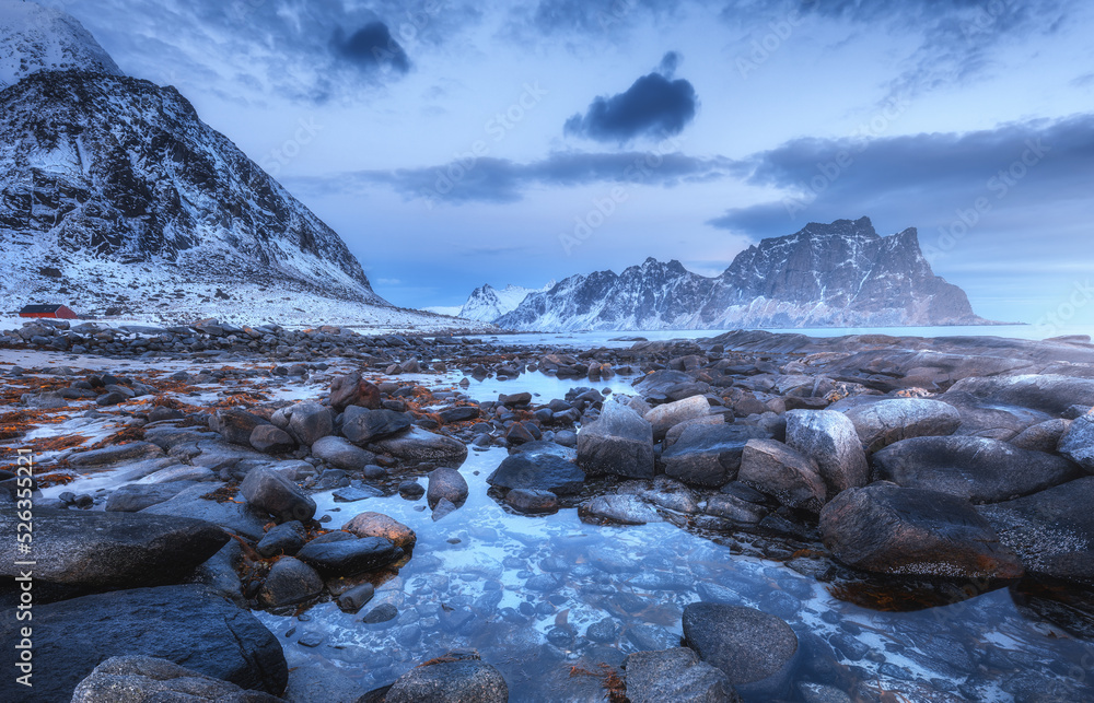 Sea coast with stones and blurred water, snowy rocky mountains