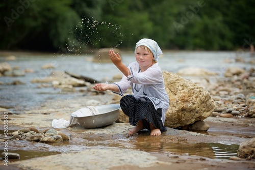 Girl in a long village vintage clothes sitting on the Bank of the river and splashing water. The river with a fast current in the country with a stone Bank.