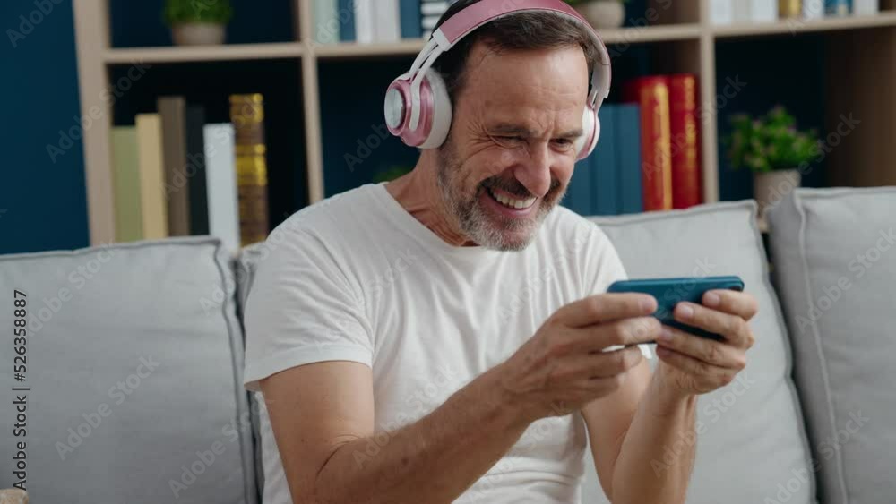 Middle age man playing video game sitting on sofa at home Middle age man playing video game sitting on sofa at home