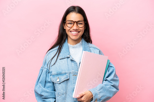 Young student Colombian woman isolated on pink background posing with arms at hip and smiling