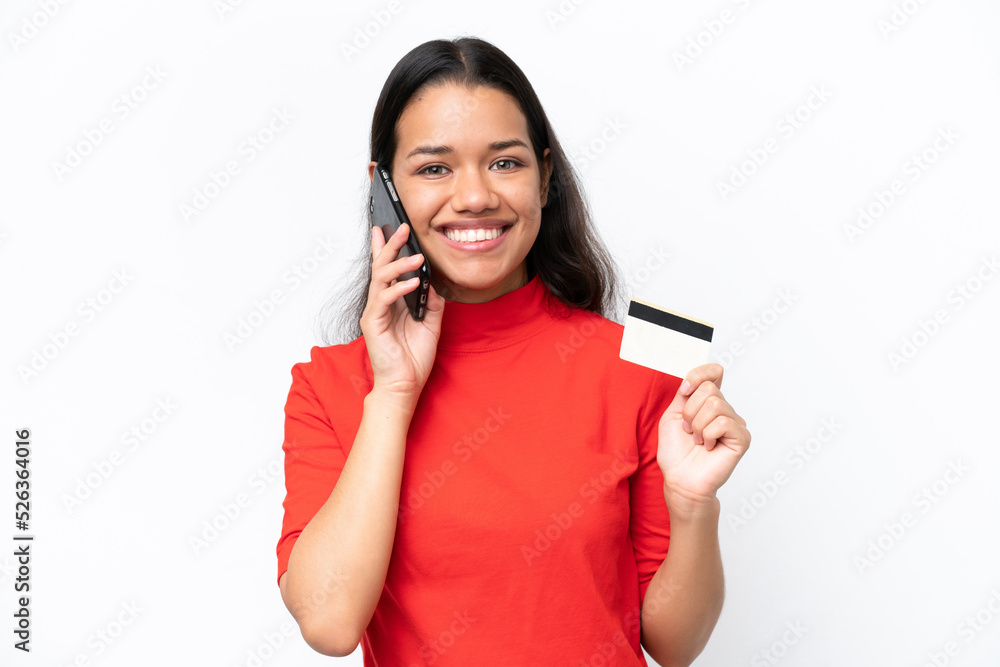 Young Colombian woman isolated on white background keeping a conversation with the mobile phone and holding a credit card