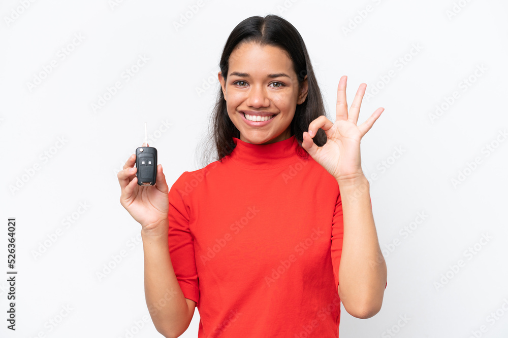Young Colombian woman holding car keys isolated on white background showing ok sign with fingers Young Colombian woman holding car keys isolated on white background showing ok sign with fingers