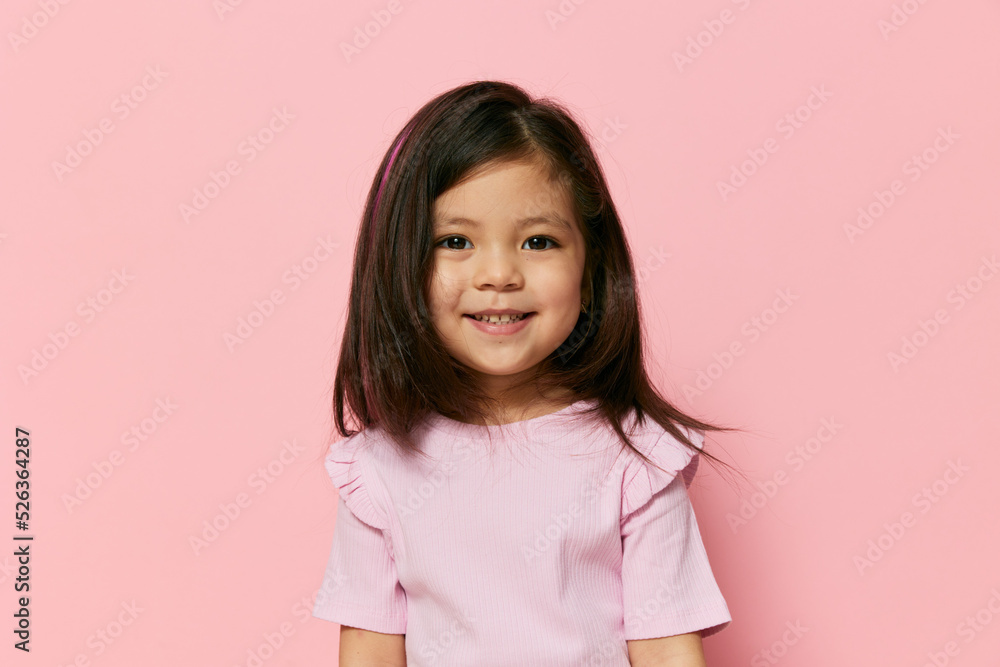 a little beautiful girl of preschool age stands on a pink background in a pink T-shirt with her hair down, looks at camera with incomprehension a little beautiful girl of preschool age stands on a pink background in a pink T-shirt with her hair down, looks at camera with incomprehension
