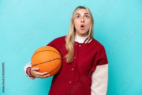 Young caucasian basketball player woman isolated on blue background looking up and with surprised expression