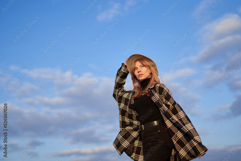 Attractive blonde long hair woman in stylish clothes - shirt and brown hat on with blue cloudy sky background. Portrait of a girl looking forward. High quality image Attractive blonde long hair woman in stylish clothes - shirt and brown hat on with blue cloudy sky background. Portrait of a girl looking forward. High quality image