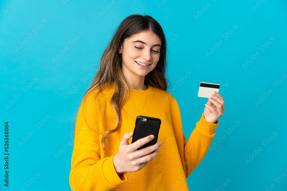 Young caucasian woman isolated on blue background buying with the mobile with a credit card Young caucasian woman isolated on blue background buying with the mobile with a credit card