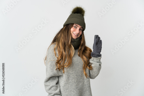 Young caucasian woman with winter hat isolated on white background saluting with hand with happy expression