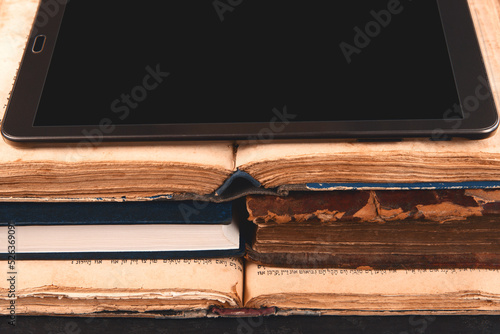 Open pages of old shabby brown and new jewish books, digital tablet. Open pages of siddur and machzor. Concept of choice between new technologies and old books. Analog vs digital. Closeup.