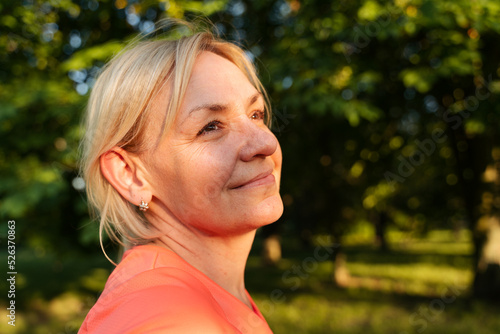 Mature blonde woman portrait in park on sunset summer day