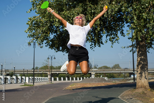 A cute sporty woman is jumping with racket and ball
