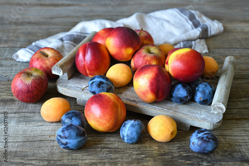 Bright summer fruits are on a tray on a rough wooden table. Nectarines  apples  apricots  plums. Still life in rustic style.