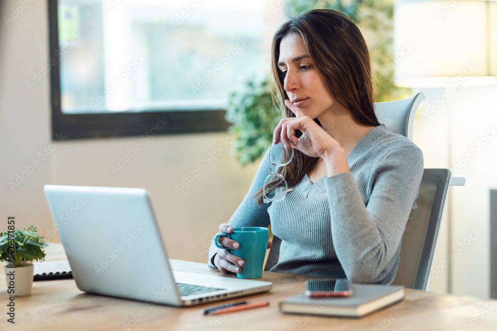 Concentrated beautiful business woman working with laptop while drinking coffee in living room at home. Concentrated beautiful business woman working with laptop while drinking coffee in living room at home.