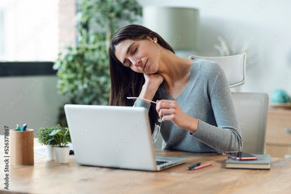 Tired business woman with neck pain looking uncomfortable while working with laptop at home.