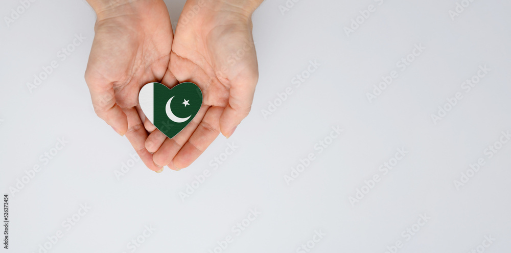 Fototapeta premium The national flag of Pakistan in the shape of a heart of arms in female hands. Flat lay, copy space.