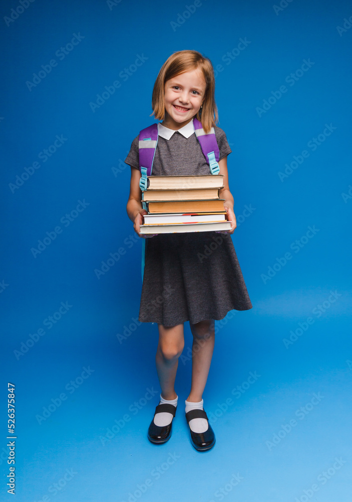 a happy teenage girl in a school uniform holds a stack of books. Banner of a schoolgirl. Portrait of a schoolgirl with space to copy on a blue background. a happy teenage girl in a school uniform holds a stack of books. Banner of a schoolgirl. Portrait of a schoolgirl with space to copy on a blue background.