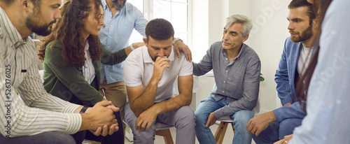 Foto Group of young and mature people supporting and comforting an upset depressed man during a group therapy session with a professional psychologist or therapist