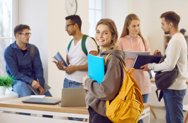 Portrait of smiling millennial Caucasian girl with backpack with groupmates in college or university. Happy young female schoolgirl satisfied with school course or training. Education concept.