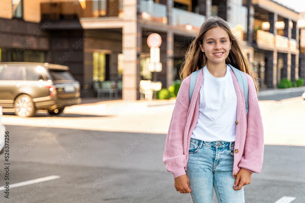 Fototapeta premium A young teenage girl goes to school with a backpack. A teenage student or a schoolgirl. The concept of education. Happy girl's face, positive and smiling emotions.