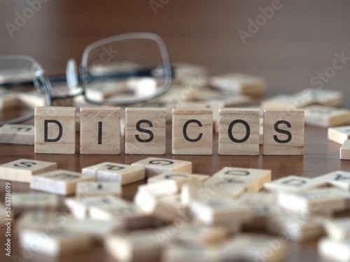 discos Wort oder Konzept dargestellt durch hölzerne Buchstabenfliesen auf einem Holztisch mit Brille und einem Buch