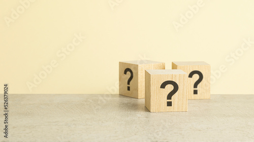 Cube with question marks on wooden background. Space for text