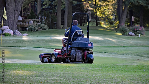 A maintenance worker mows a green, in the early morning hours, on a golf course.