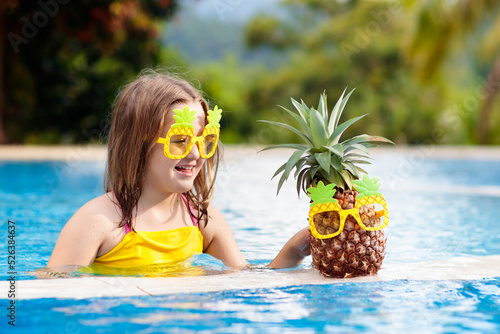 Child with pineapple in swimming pool. Kids swim.