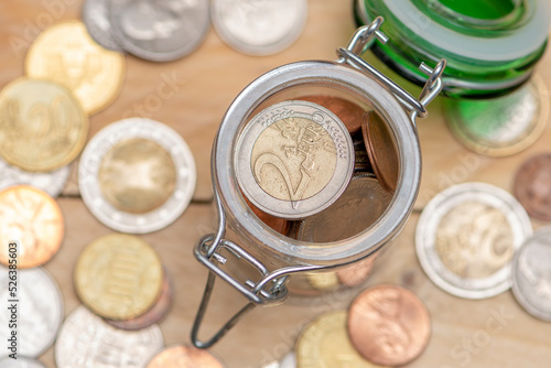 An open jar with small coins stands on a wooden table, scattered euro cents, top view, close-up, selective focus. A concept for business and finance, savings and price increases.