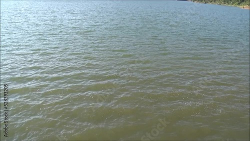 The murky, small waves, on the large lake surrounded by dense forest on the hills.