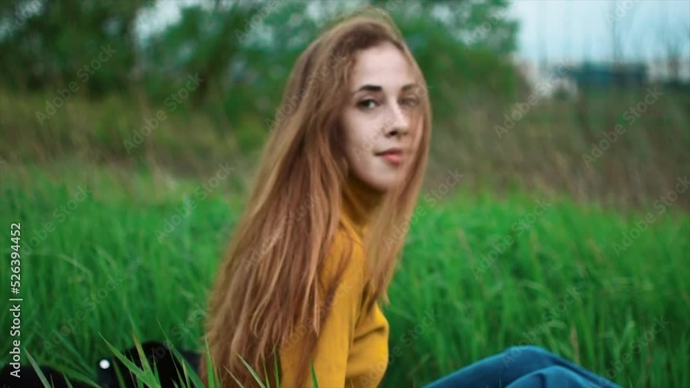 Close-up portrait of a beautiful girl sitting in the grass and looking sensually into the frame while the wind plays in her hair Close-up portrait of a beautiful girl sitting in the grass and looking sensually into the frame while the wind plays in her hair