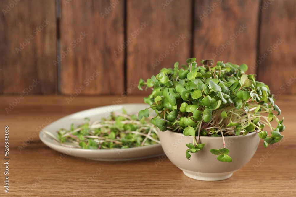 Fresh radish microgreens in bowl on wooden table, space for text Fresh radish microgreens in bowl on wooden table, space for text