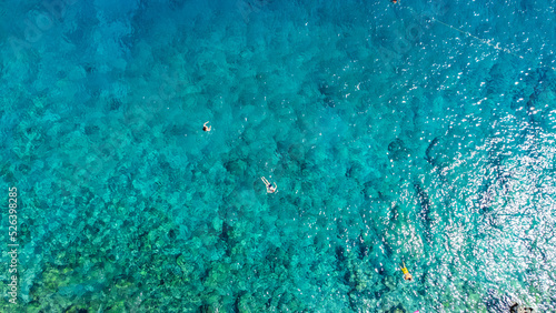 Drone photo of a people enjoying a swim in the turquoise sea at the remote beach surrounded by the cliffs in the Turkish Riviera