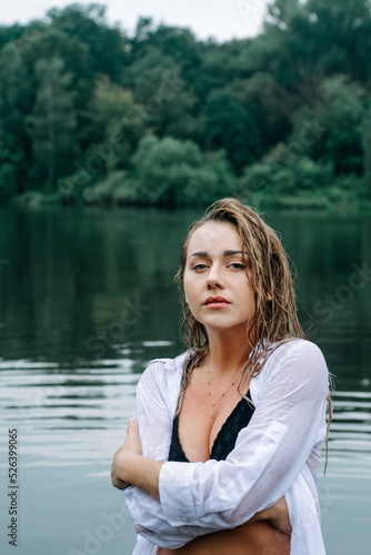 Beautiful sensual blonde girl with wet hair in a white shirt and black swimsuit posing in the lake after the rain. Magic beauty. Forest witch. © Wild Garden