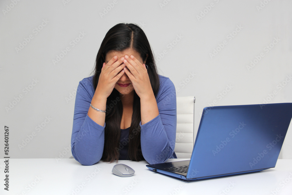 Dark-haired latin adult woman works in her office with laptop with a lot of stress having a headache with a migraine and suffering from tiredness, depression, anxiety and burnout Dark-haired latin adult woman works in her office with laptop with a lot of stress having a headache with a migraine and suffering from tiredness, depression, anxiety and burnout
