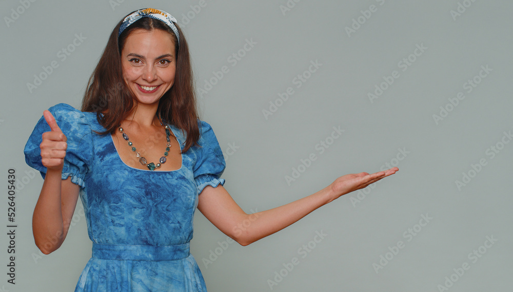 Lovely pretty young woman showing thumbs up and pointing right empty place, advertising area for commercial text, copy space for goods promotion. Adult stylish girl isolated on gray studio background Lovely pretty young woman showing thumbs up and pointing right empty place, advertising area for commercial text, copy space for goods promotion. Adult stylish girl isolated on gray studio background