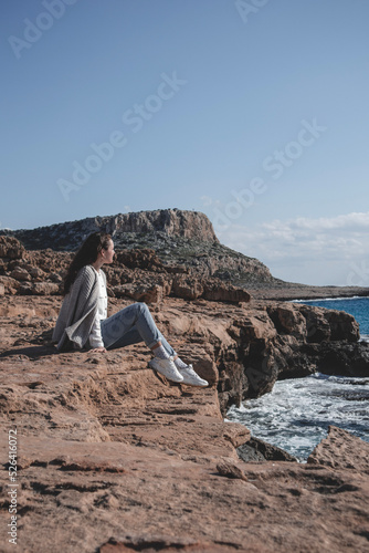 Young woman is sitting in front of Cape Greco mountain and looking at seashore