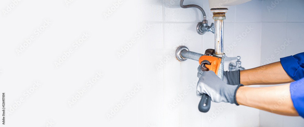 Technician plumber using a wrench to repair a water pipe under the sink. Concept of maintenance, fix water plumbing leaks, replace the kitchen sink drain, cleaning clogged pipes is dirty or rusty. Technician plumber using a wrench to repair a water pipe under the sink. Concept of maintenance, fix water plumbing leaks, replace the kitchen sink drain, cleaning clogged pipes is dirty or rusty.