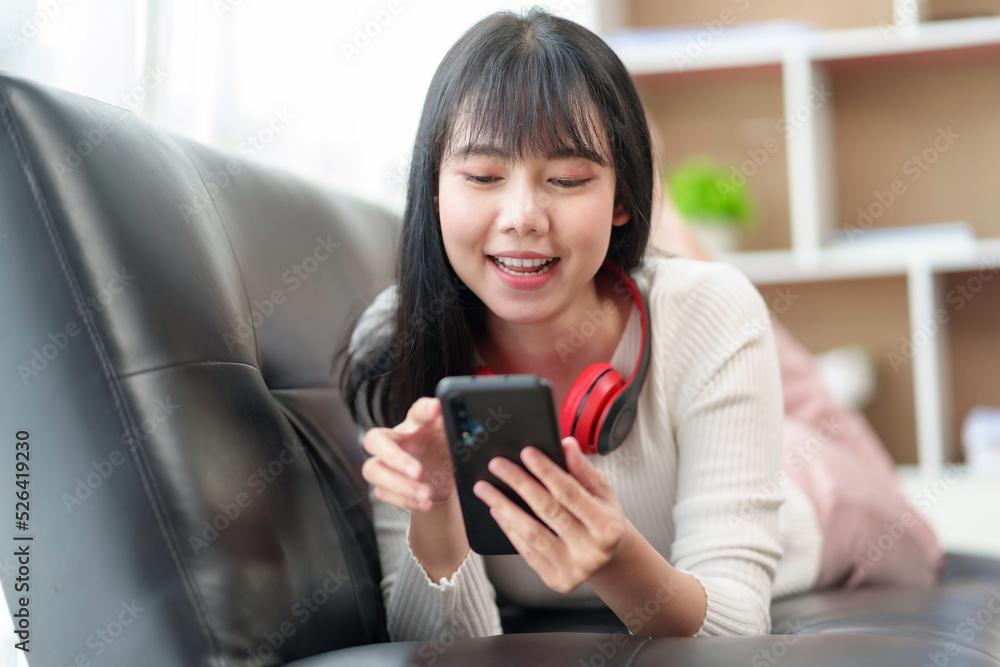 Pretty and cute Asian woman relaxing on the sofa, playing social media and accessing apps various entertainments, wear headphones, listen to music happily at home. Pretty and cute Asian woman relaxing on the sofa, playing social media and accessing apps various entertainments, wear headphones, listen to music happily at home.