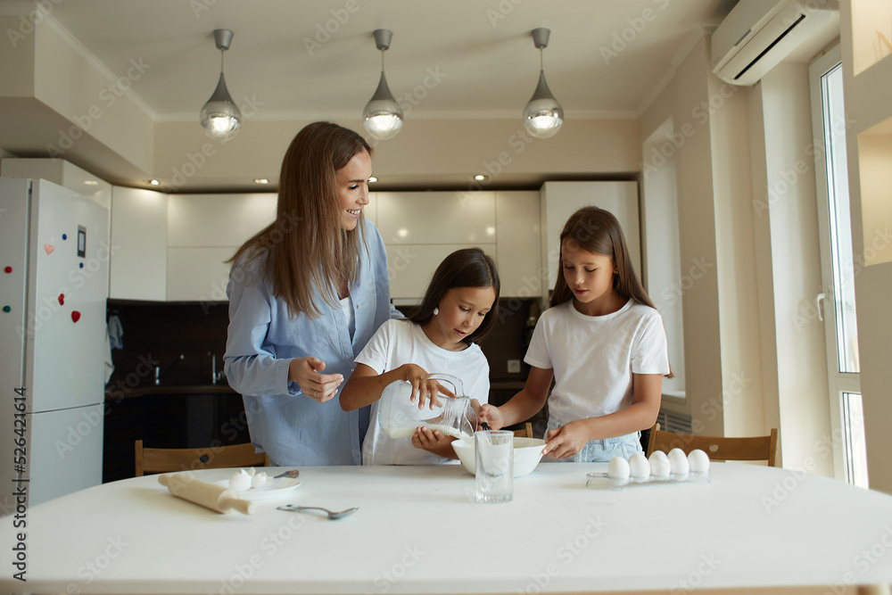 Happy family preparing food together in the kitchen. Mom teaches her daughters how to cook and knead the dough. Mother's Day concept. family dinner