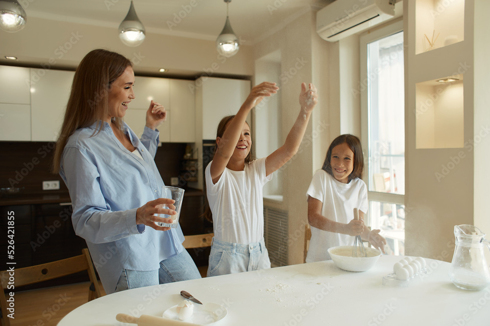 young beautiful mother teaches her daughters how to cook dough in the kitchen. They play with flour. family breakfast young beautiful mother teaches her daughters how to cook dough in the kitchen. They play with flour. family breakfast